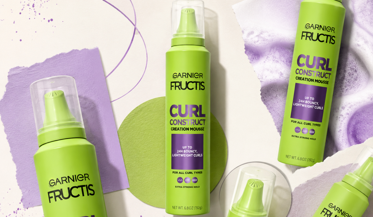 A lime-green Garnier Fructis Curl Construct Creation Mousse bottle appears in an editorial-style collage with multiple cropped product cutouts, lavender paper textures, purple graphic accents and soft studio shadows on a cream background