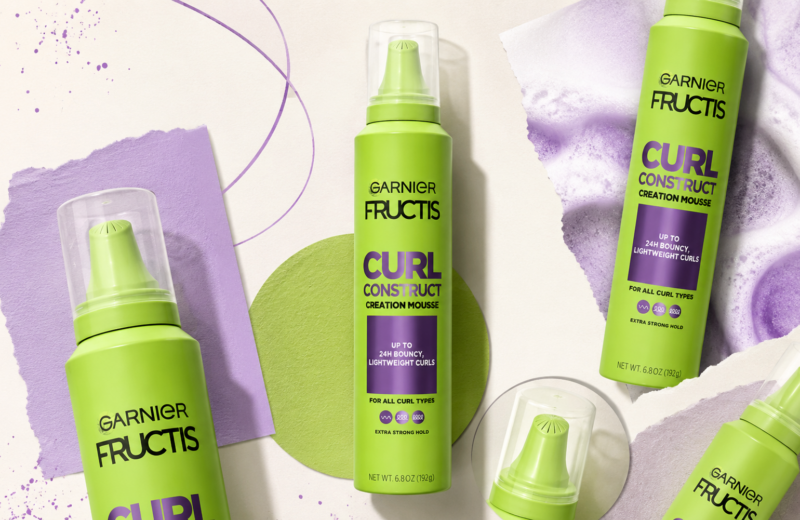 A lime-green Garnier Fructis Curl Construct Creation Mousse bottle appears in an editorial-style collage with multiple cropped product cutouts, lavender paper textures, purple graphic accents and soft studio shadows on a cream background