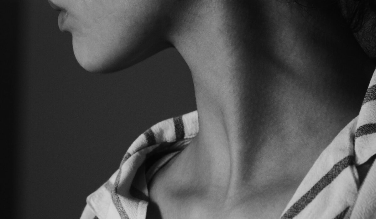 Black-and-white close-up of a person’s neck and jawline, with their head tilted upward and a striped shirt visible at the shoulders.