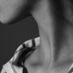 Black-and-white close-up of a person’s neck and jawline, with their head tilted upward and a striped shirt visible at the shoulders.