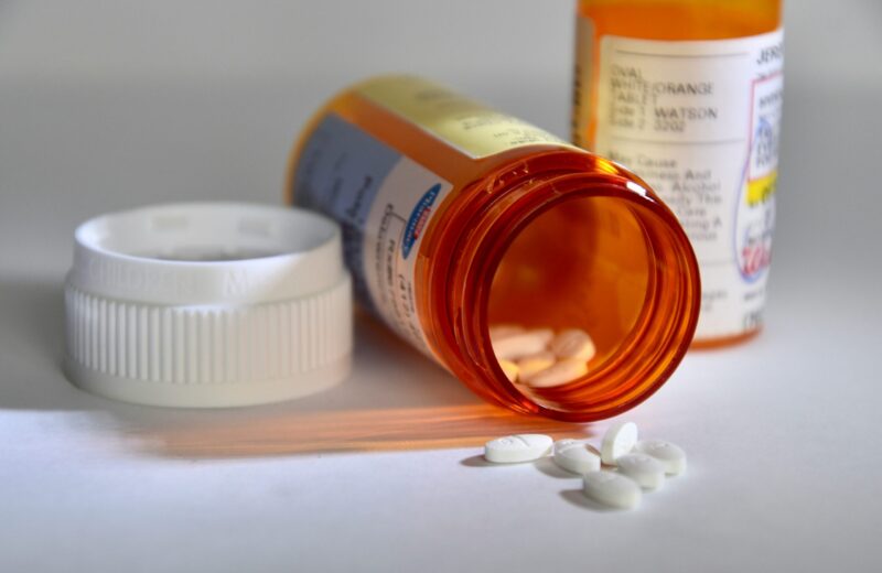 A pill container lies on its side with white pills spilling out