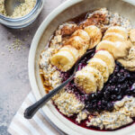 bowl of oatmeal topped with seeds, banana, blueberries, and nut butter